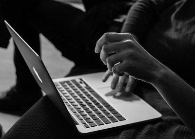 A black & white image of a person using a laptop on their legs