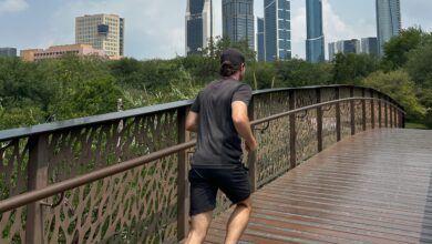Male running over a wooden bridge in a park with a city in the far background.