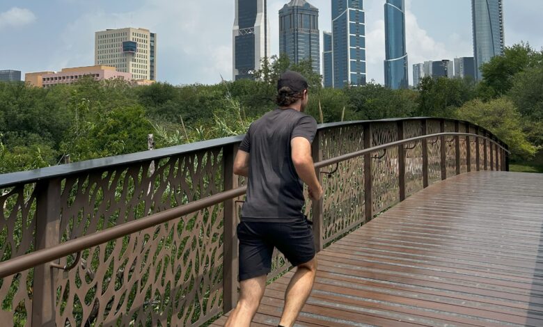 Male running over a wooden bridge in a park with a city in the far background.